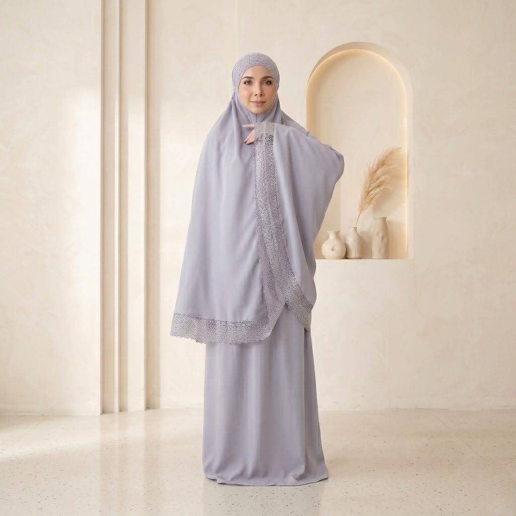 Woman wearing a light gray traditional outfit with a matching hijab in a minimalistic setting.